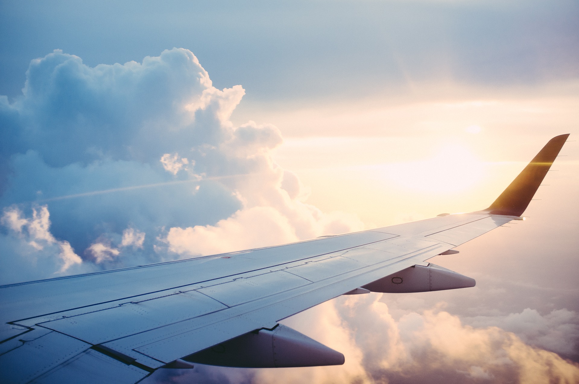 Photo from airplane in the sky looking out the window at clouds and a plane wing